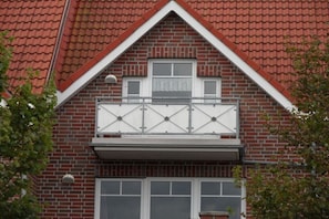 A two-story building with a red-tiled roof, a balcony with a metal railing, and a brick facade. - Holiday apartment with 1 bedroom (Dornum-Neßmersiel)
