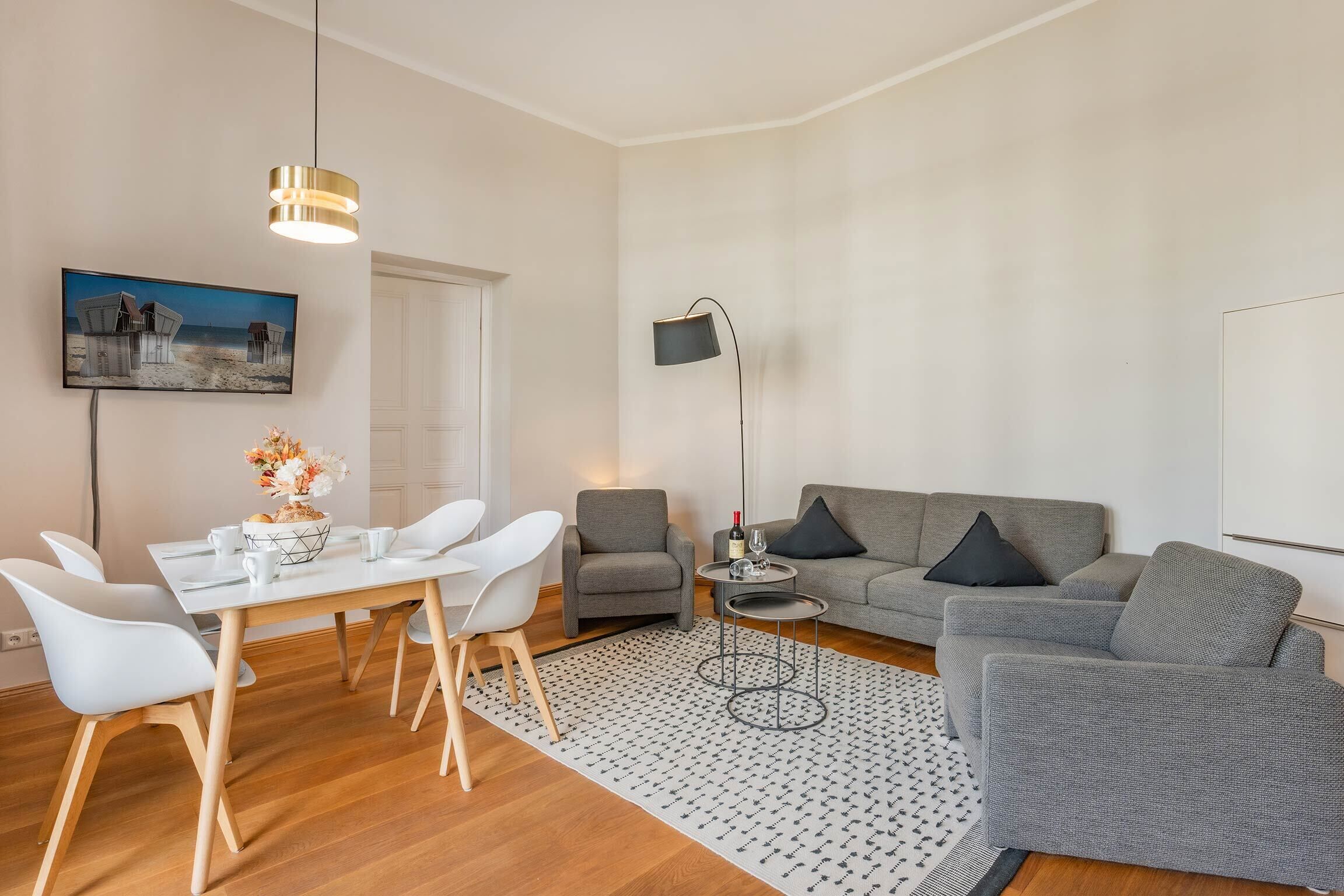 Een moderne woonkamer met een eettafel, stoelen, een grijze bank, een vloerlamp en een schilderij aan de muur.