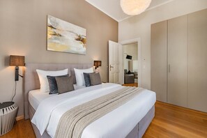 Ein Schlafzimmer mit Bett, Nachttischlampen, einem großen abstrakten Gemälde, einem Kleiderschrank und einer Tür zu einem weiteren Raum.