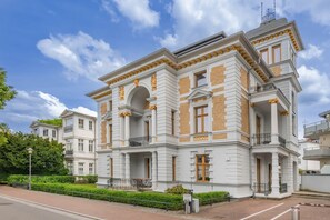 Un immeuble à plusieurs étages, doté d’une architecture classique, avec des colonnes, des balcons et une façade symétrique.