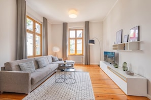 Ein modernes Wohnzimmer mit einem grauen Sofa, einem Couchtisch, einem Fernseher auf einem weißen Schrank und einer Stehlampe.