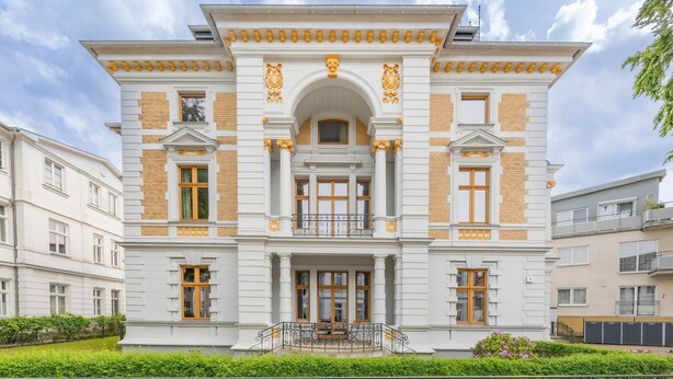 Um edifício grande e branco com um arco central, colunas e detalhes decorativos.