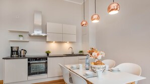 Cozinha moderna com armários brancos, forno embutido e área de refeições com mesa e cadeiras brancas.