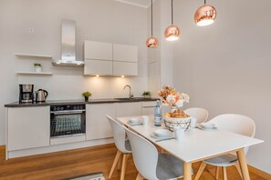 Eine moderne Küche mit weißen Schränken, einem Einbauofen und einem Essbereich mit weißem Tisch und Stühlen.