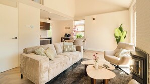 Un salon comprenant un canapé, un fauteuil, une table basse, une cheminée, et un coin cuisine à l’arrière-plan.