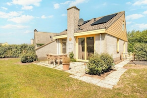 Ein Haus mit Backsteinfassade, Schornstein, einer Solaranlage, einer Terrasse mit Tisch und Stühlen sowie einem Garten.