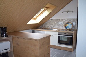 Eine kleine Küche mit Dachfenster, einer Kaffeemaschine, einem Spülbecken und einem Backofen.