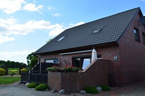 Ein Ziegelhaus mit geneigtem Dach, einer Satellitenschüssel und einem kleinen Garten mit Blumen.