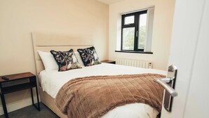 Una camera da letto con un letto, cuscini, un comodino, una finestra e un termosifone.