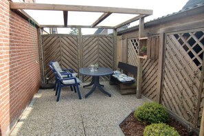 Eine Terrasse mit einem runden Tisch und zwei blauen Stühlen, einem Holzzaun und einer Ziegelwand.