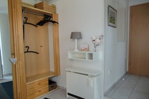Ein Zimmer mit einem Holzschrank, einem weißen Heizkörper, einem Regal mit einer Lampe und einem gerahmten Bild an der Wand.