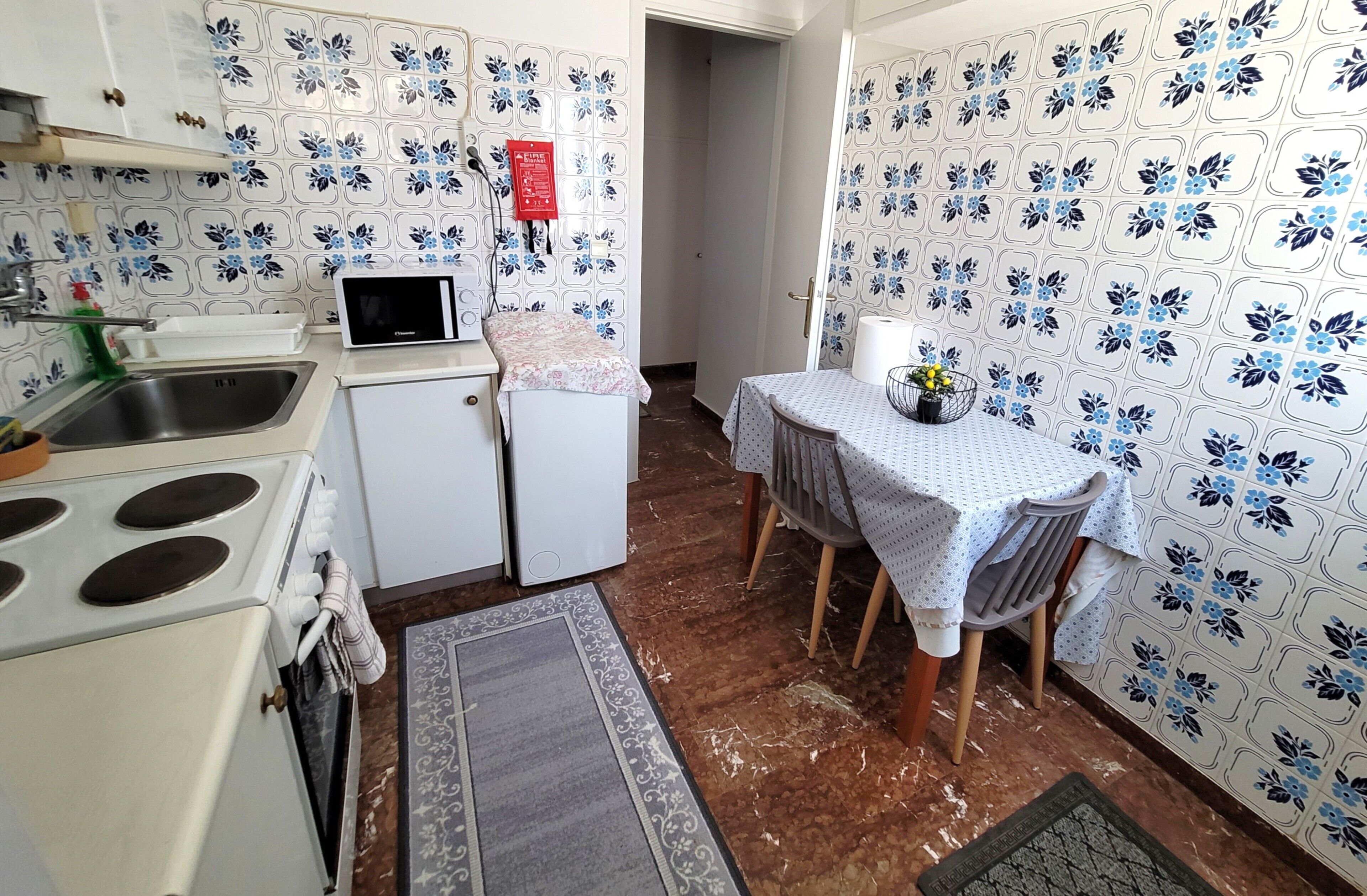 A compact kitchen with a stove, microwave, and sink, a small refrigerator, and a dining area with a table and chairs.