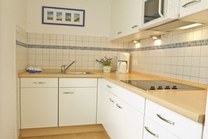 Eine Küche mit weißen Schränken, einer Holzausziehtafel, einer Spüle, einem Herd und einer Mikrowelle.