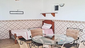 Ein Zimmer mit einem Bett, einem kleinen Fernseher und einem Glastisch mit Korbstühlen.