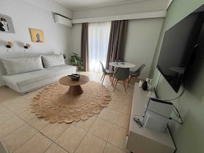 Ein modernes Wohnzimmer mit Sofa, Couchtisch, Essbereich und einem Flachbildfernseher.