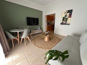 Ein Wohnzimmer mit Fernseher, Esstisch, Stühlen, Couchtisch und einer Pflanze.