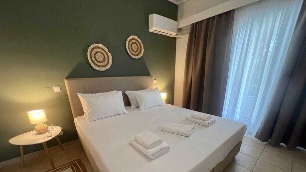 A hotel room with a large bed, two wall-mounted air conditioners, a bedside lamp, and a view of the outdoors through curtains. - Residence City Escape 202 (Rhodes)