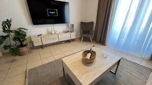 Una sala de estar moderna con un televisor de pantalla plana, un sofá, una mesa de centro, una planta en maceta y una silla.