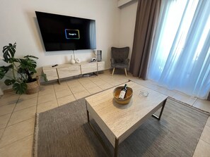 Ein modernes Wohnzimmer mit Flachbildfernseher, einer Couch, einem Couchtisch, einer Topfpflanze und einem Sessel.