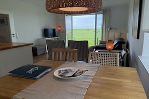 Ein Zimmer mit Esstisch, Stühlen, Fernseher und Blick ins Freie.