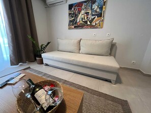 A living room with a sofa, a painting, a plant, and a table with a wine bottle and glass. - Residence City Skippers 205 (Rhodes)