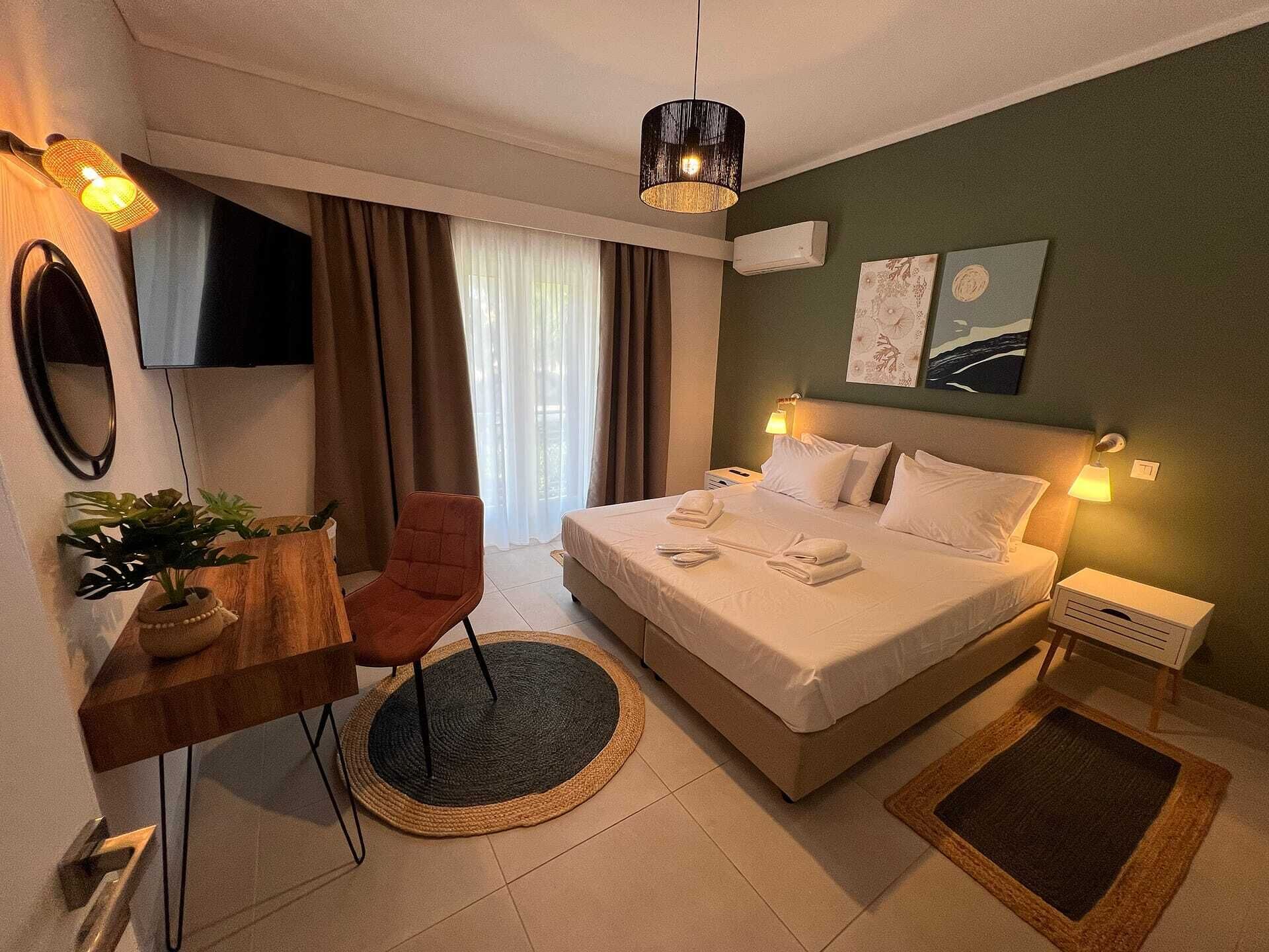 A hotel room with a bed, bedside lamps, a desk with a chair, a TV, and a plant.