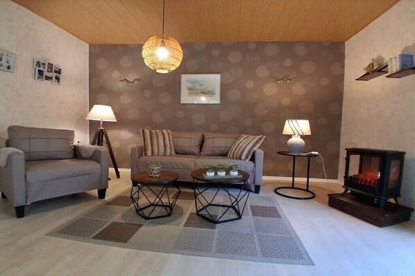 A living room with a sofa, two armchairs, a coffee table, a fireplace, and a patterned wall. - Little Seal Paradise (Moorweg)