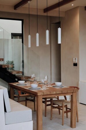 A modern dining area with a wooden table set for four, hanging pendant lights, and a glass partition. - Maison Kala (Cemagi)