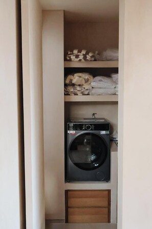 Un cuarto de lavandería con una lavadora de carga frontal, repisas con ropa doblada y un armario de madera.