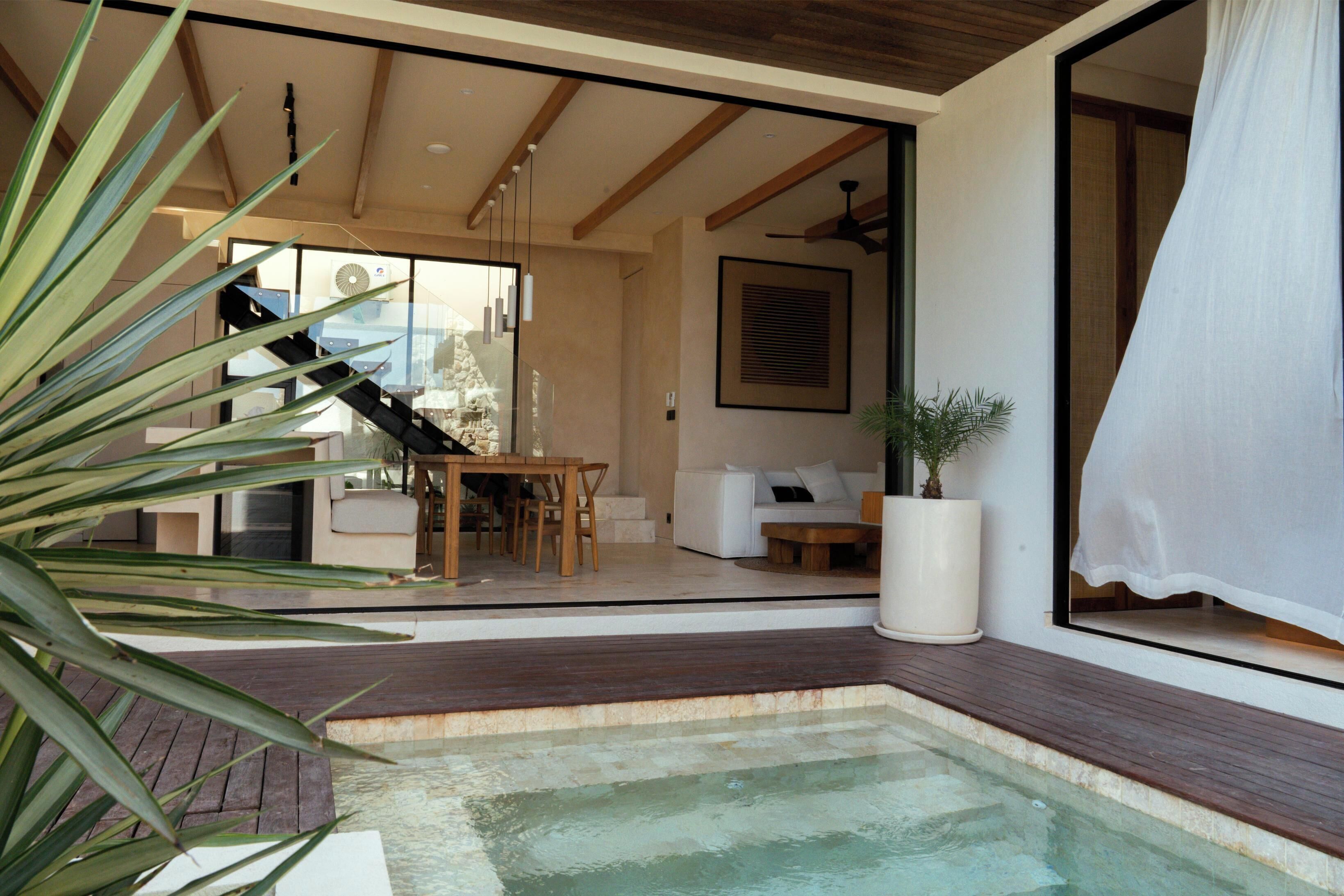 A modern interior with a pool, wooden flooring, a dining area, and a staircase leading to an upper level.