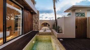 A modern outdoor pool area with a stone wall, wooden deck, and a glass-enclosed room.