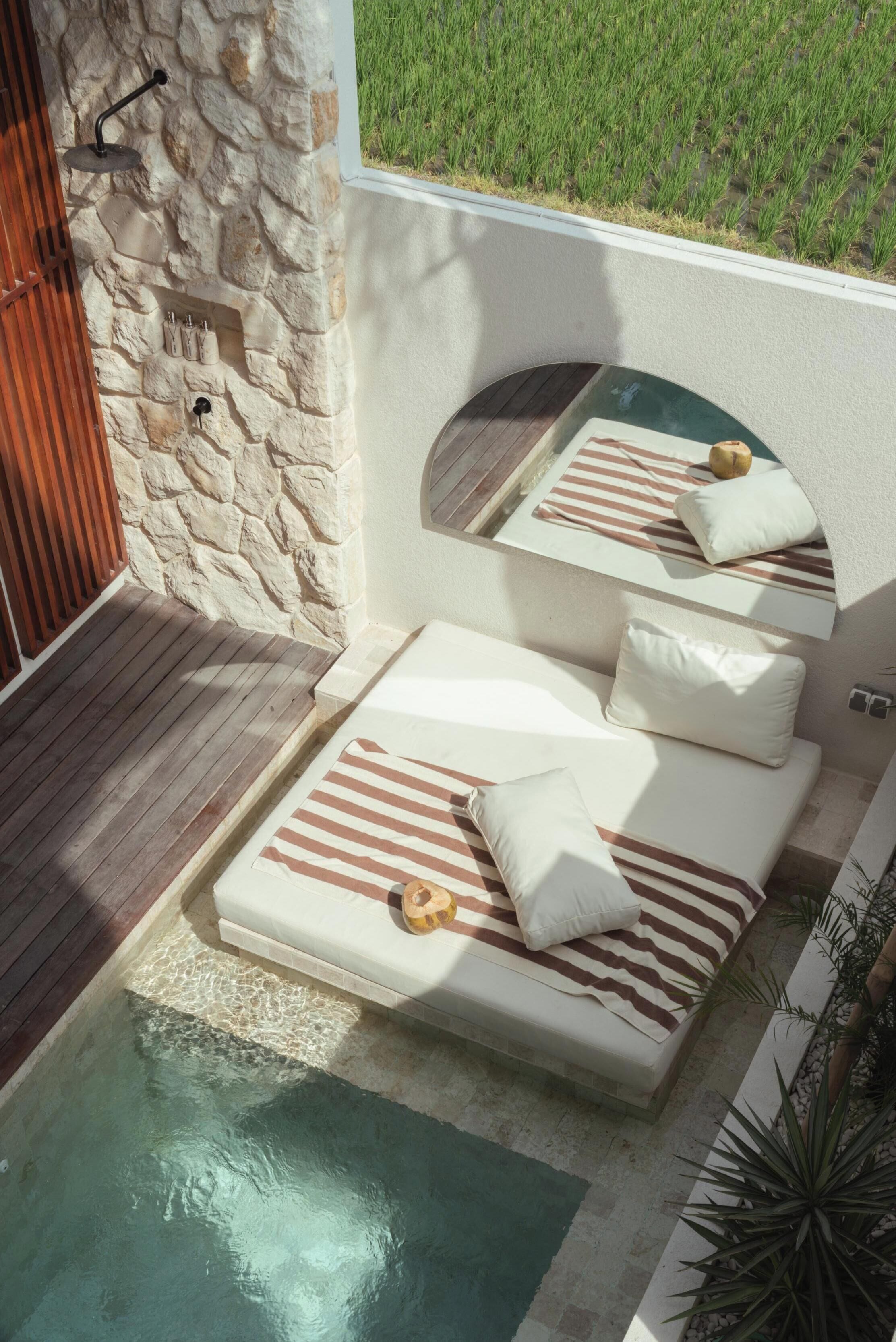 A stone wall with a built-in seating area, a small pool, and a view of a grassy field.
