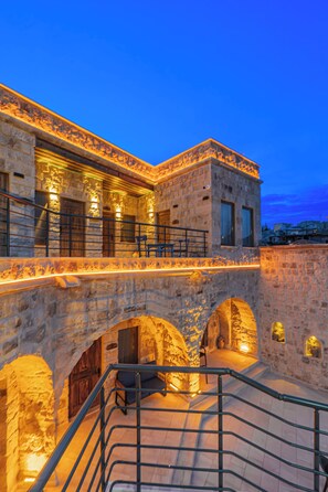 A stone building with a balcony, arched passageways, and outdoor seating.