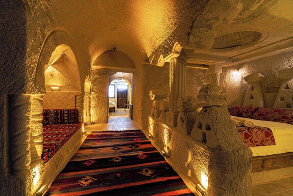 A narrow passageway with stone walls, a carpeted bench, and a bed with patterned bedding.