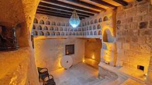 Una habitación con paredes de piedra, un candelabro, nichos abovedados, una chimenea y un techo de madera.