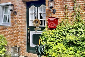 A brick house with a green door, white-framed windows, a red mailbox, and a wreath on the door. - Holiday home with 1 bedroom (Krummhörn-Loquard)