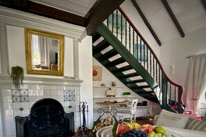 A living room with a fireplace, a staircase, and a dining area with a table set for a meal. - Holiday home with 1 bedroom (Krummhörn-Loquard)