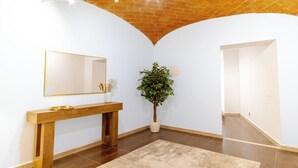 Ein Zimmer mit einem Holzkonsolentisch, einem großen Spiegel, einer Topfpflanze und einer Ziegeldecke.