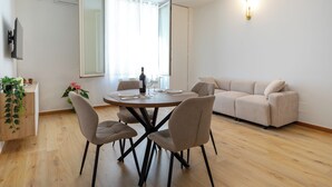 Ein modernes Wohnzimmer mit Esstisch, Stühlen, einer Couch und einem an der Wand befestigten Fernseher.