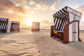 Strandstühle mit gestreifter Markise und der Aufschrift 410, auf einem Sandstrand mit Blick auf den Ozean.