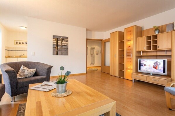 Ein modernes Wohnzimmer mit Couchtisch aus Holz, einer grauen Couch, einem Fernseher und eingebauten Holzregalen.