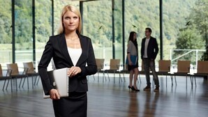 A woman in a black suit holding a laptop in a spacious room with large windows and a view of trees. - Hotel Wesenufer (Wesenufer)