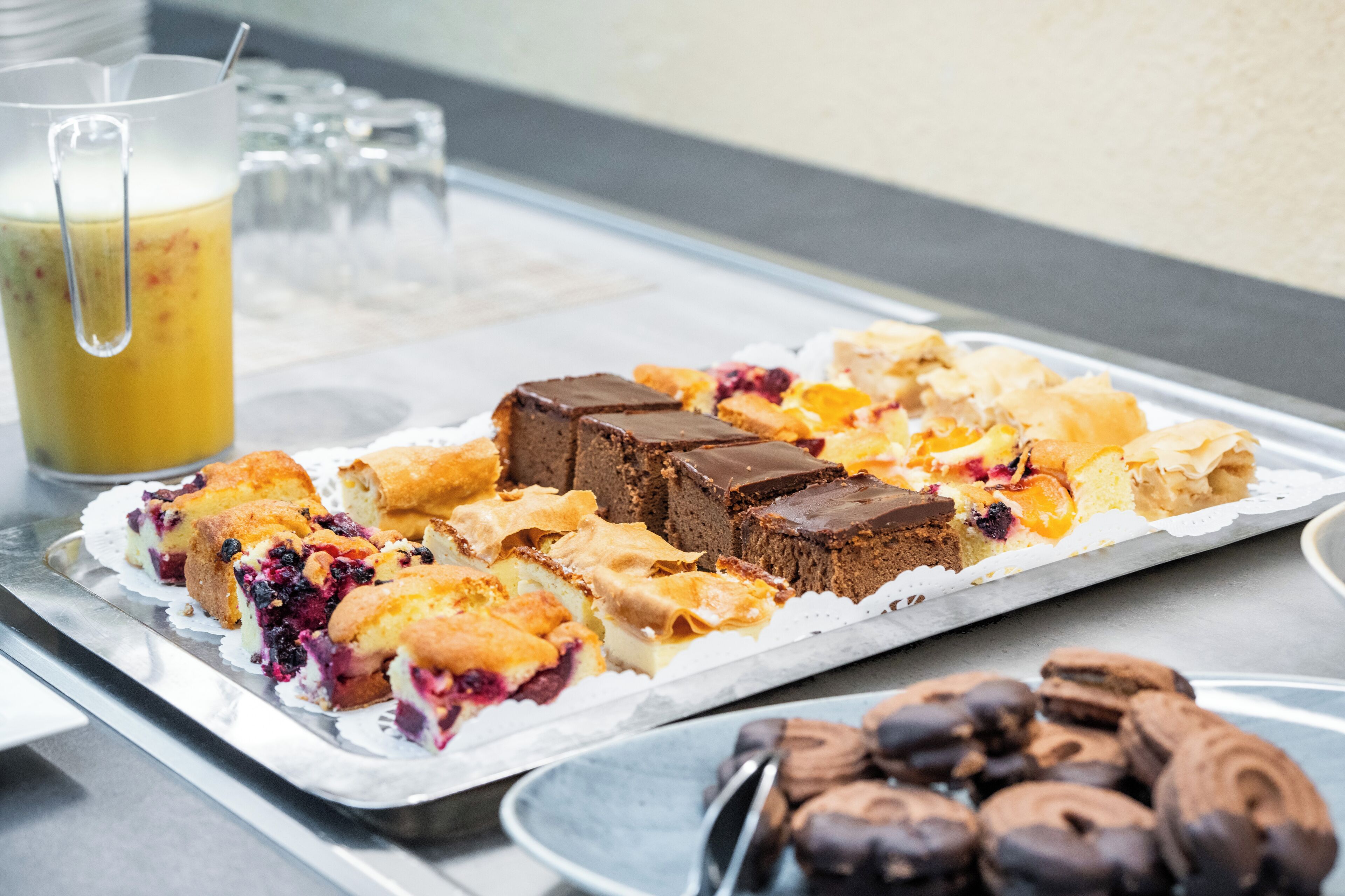 A tray of assorted desserts and a glass of juice on a table.