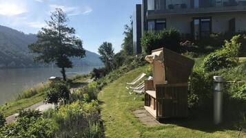 Un edificio moderno con balcón, un área verde con sillones de descanso y vistas a un lago.