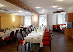 Un comedor con mesas largas, sillas y una zona de cocina.