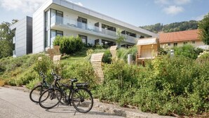 A modern building with a flat roof, large windows, and a balcony. There are bicycles parked in front. - Hotel Wesenufer (Wesenufer)