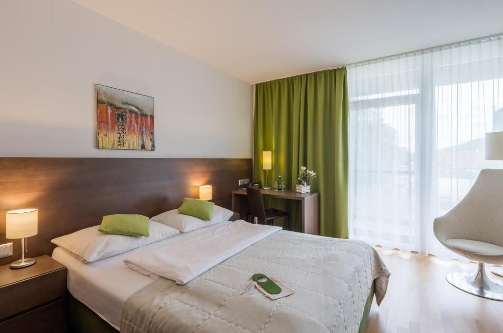 Habitación de hotel con cama, lámparas de noche, escritorio, una silla y un cuadro en la pared.