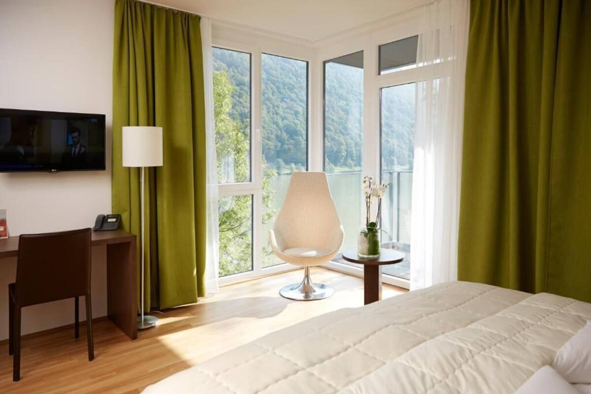 Ein Hotelzimmer mit Bett, Schreibtisch, Stuhl, Fernseher und Blick ins Freie.