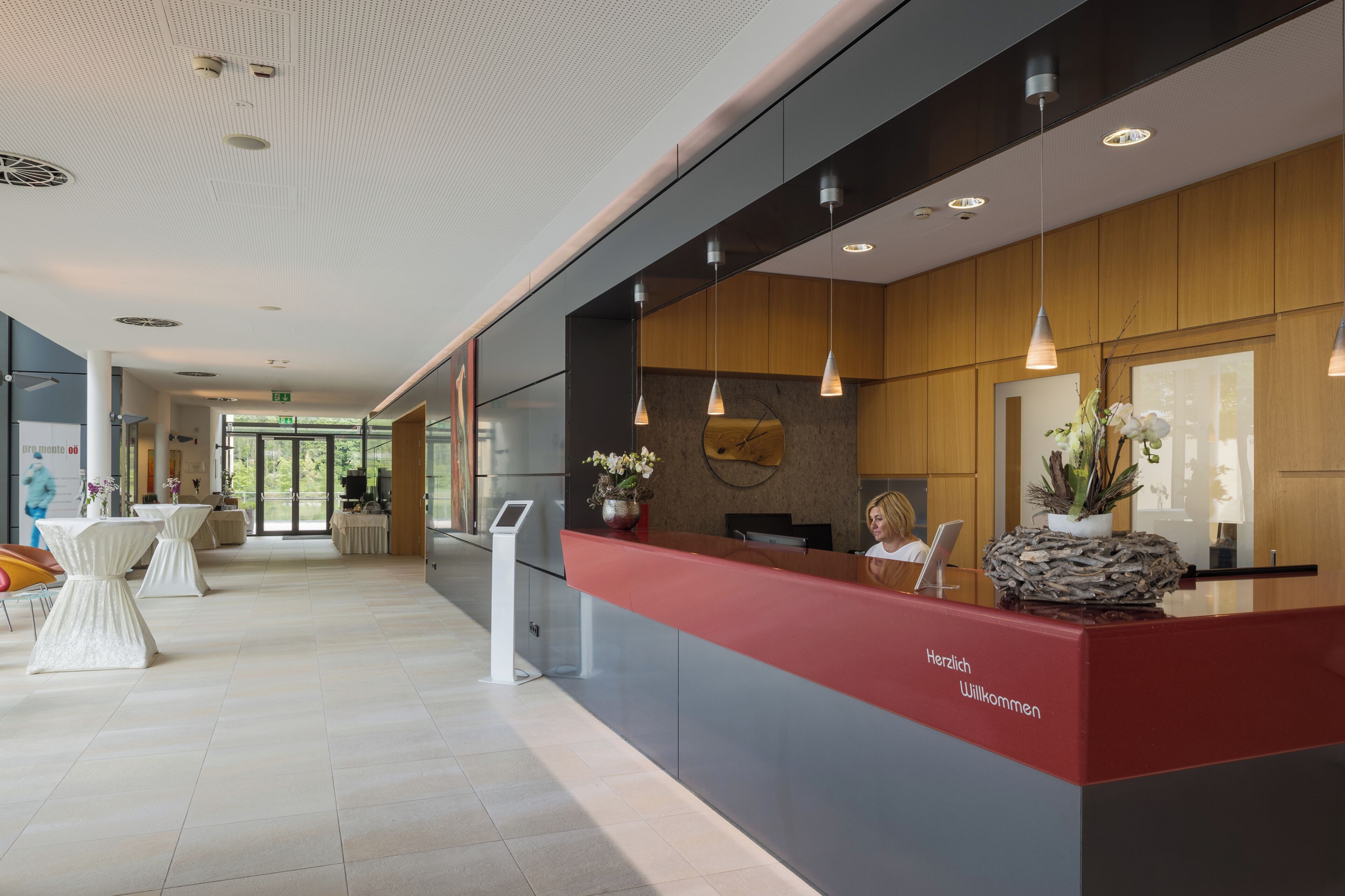 A modern reception area with a red counter, white tables, and pendant lighting.