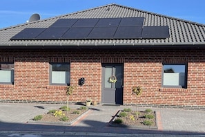 A brick building with a flat roof, solar panels, a door with a wreath, and small plants in front. - Holiday home in Pewsum with swimming pool (Pewsum)
